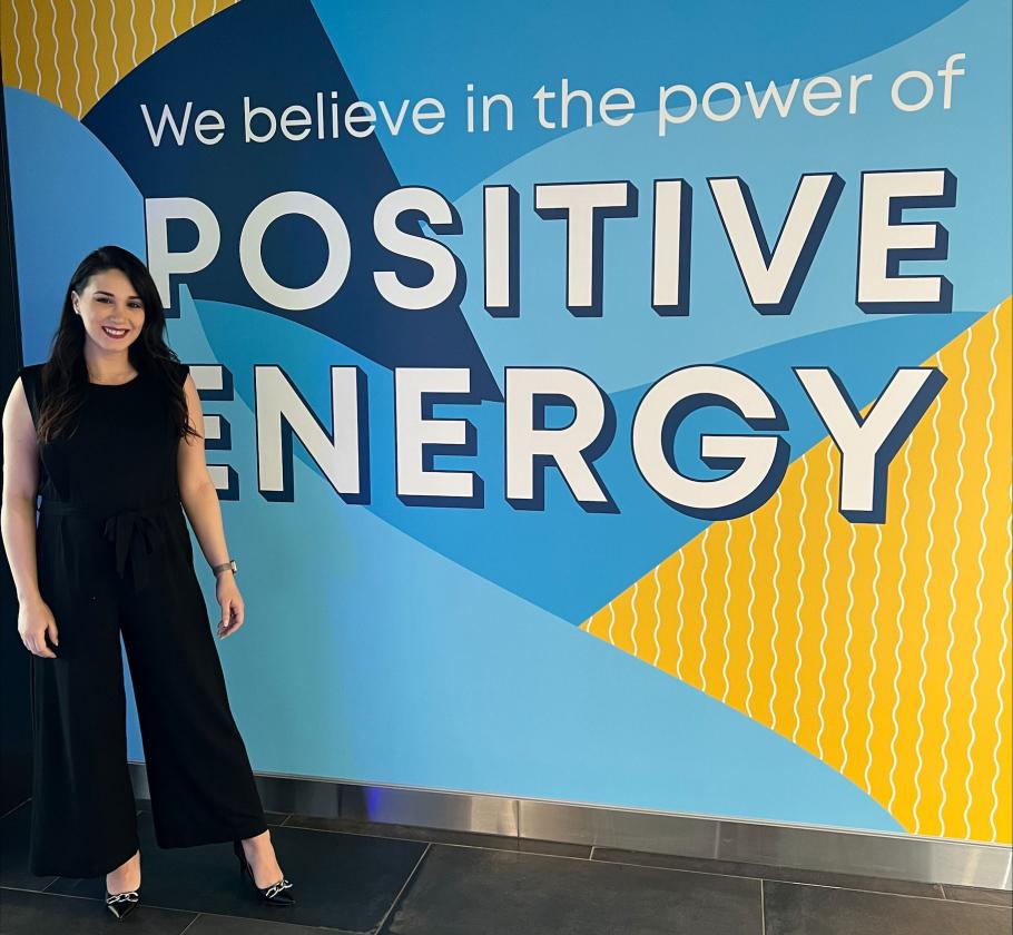 NFE Employee standing by sign reading "we believe in the power of positive energy"